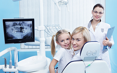 A young child and mom sitting in a dental chair looking at an x-ray
