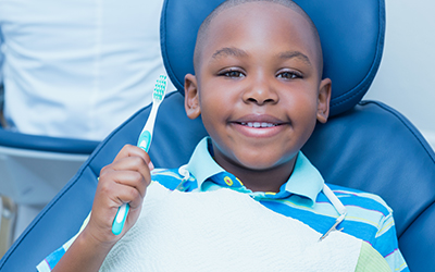 A young boy sitting in a dental chair smiling with a toothbrush